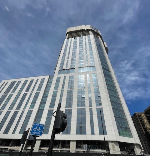 Tall modern glass tower block photographed from street level against a blue sky